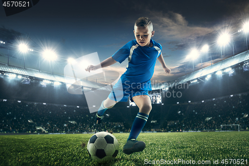 Image of Young boy with soccer ball doing flying kick at stadium