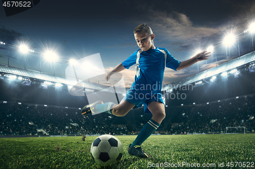 Image of Young boy with soccer ball doing flying kick at stadium