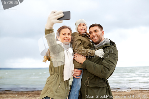 Image of family taking selfie by smartphone on autumn beach