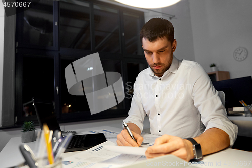 Image of businessman with papers and laptop at night office