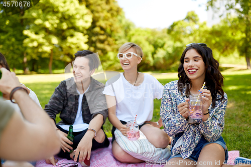 Image of happy friends with drinks at picnic in summer park