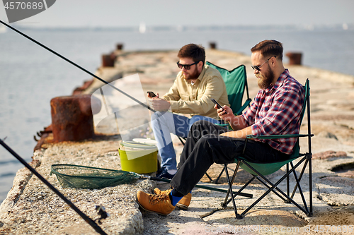 Image of friends with smartphones fishing on pier at sea