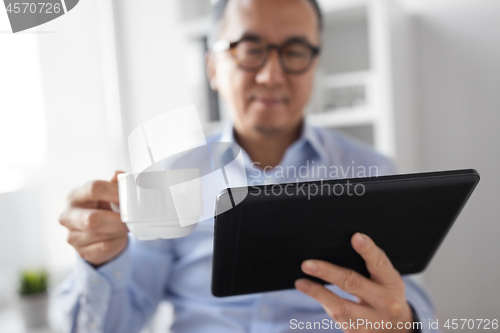 Image of businessman with tablet pc drinks coffee at office