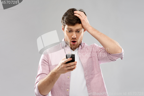 Image of embarrassed young man looking at smartphone