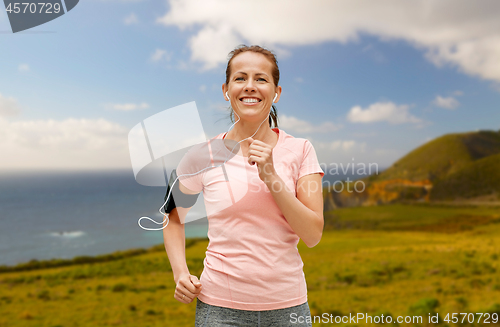 Image of woman with earphones and armband running outdoors