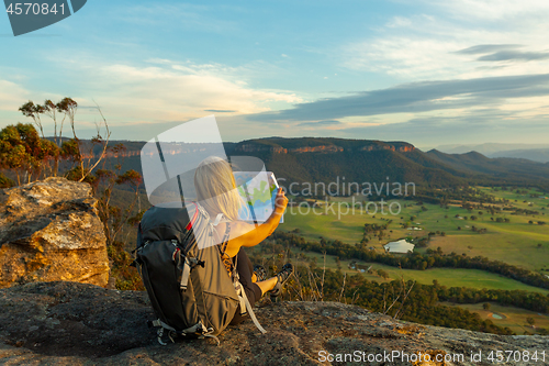 Image of Hiker or tourist sitting on a rock using a map