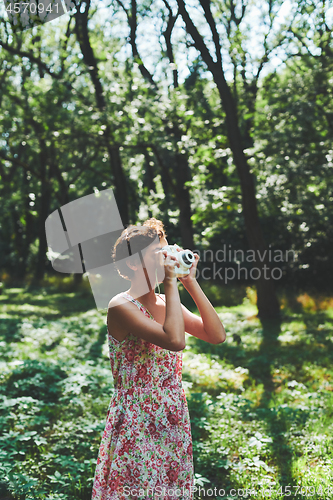 Image of Active girl taking photo on instant camera in sunny forest