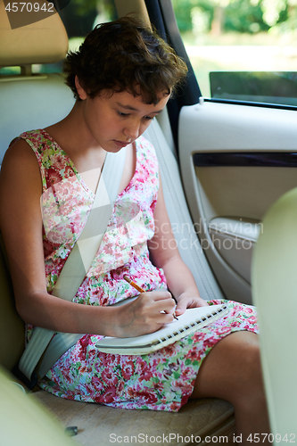 Image of Thoughtful girl drawing in sketchbook in back seat of car