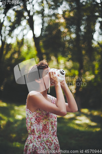 Image of Active girl taking photo on instant camera in sunny forest