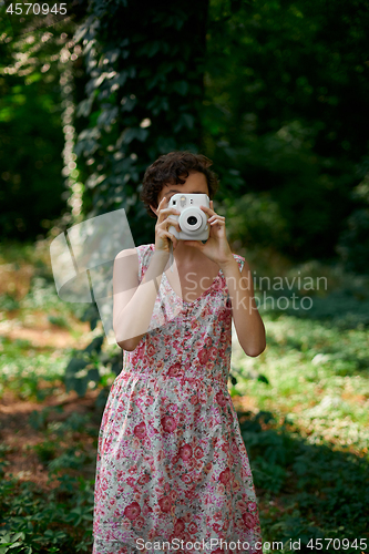 Image of Smiling girl taking photo on instant camera in forest