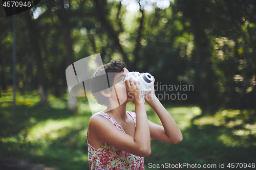 Image of Active girl taking photo on instant camera in sunny forest