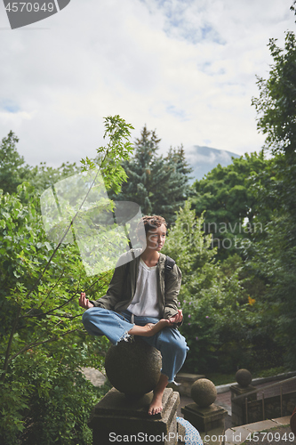 Image of Girl sitting in meditating posture on sculpture ball of fence in park