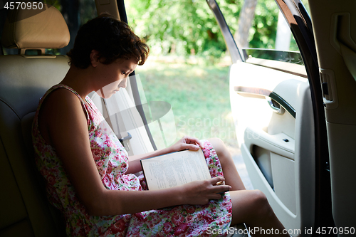 Image of Enthusiastic girl reading book in car in trip