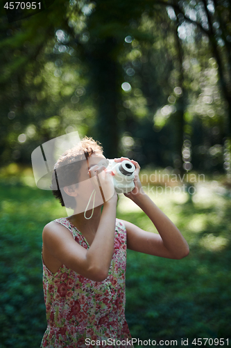 Image of Active girl taking photo on instant camera in sunny forest