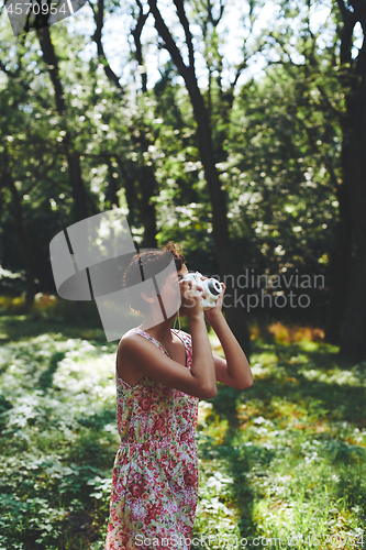 Image of Active girl taking photo on instant camera in sunny forest