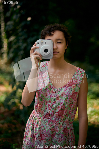 Image of Smiling girl taking photo on instant camera in forest