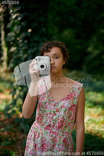 Image of Smiling girl taking photo on instant camera in forest