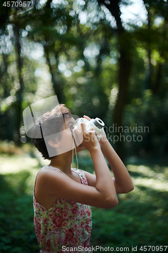 Image of Active girl taking photo on instant camera in sunny forest