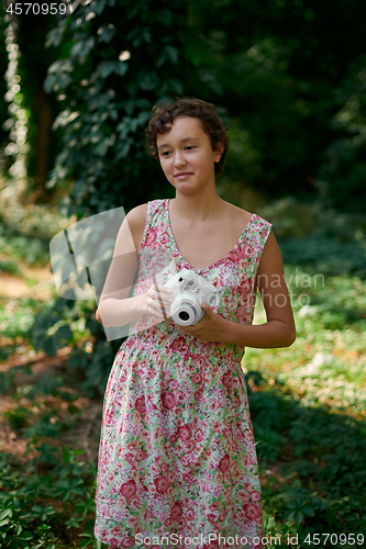 Image of Smiling girl taking photo on instant camera in forest