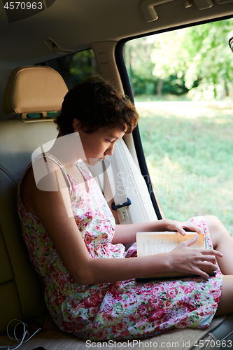 Image of Enthusiastic girl reading book in car in trip