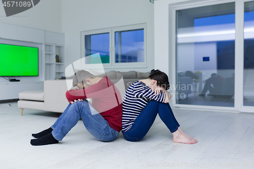 Image of young couple sitting with back to each other on floor