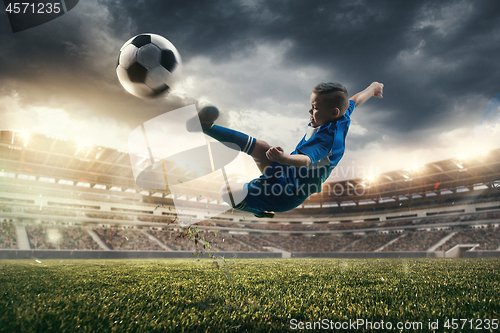 Image of Young boy with soccer ball doing flying kick at stadium