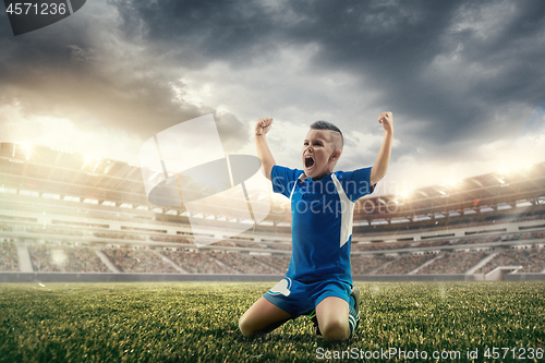 Image of Young boy with soccer ball doing flying kick at stadium