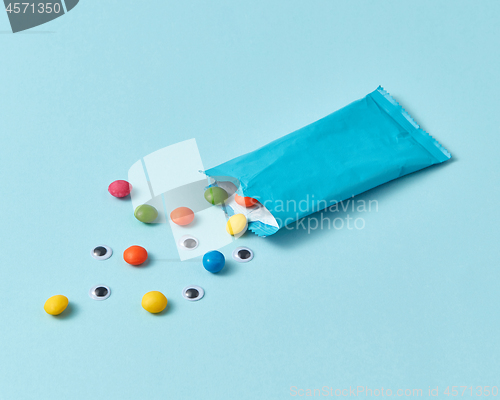 Image of Paper box with colorful candy and pupils on a light blue background.