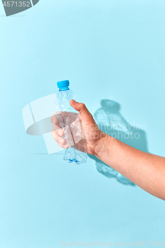 Image of Hand crushes plastic bottle with shadow on a light blue.