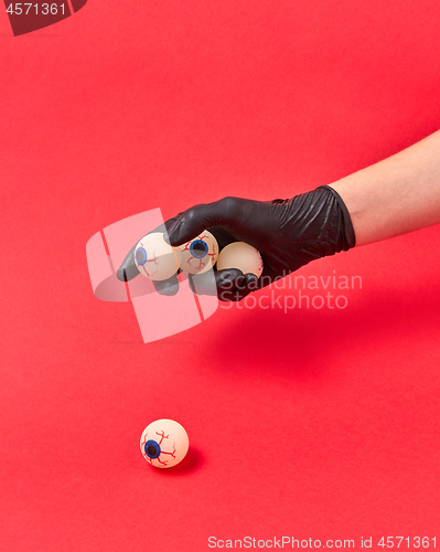 Image of Woman hand in black glove with human eyeballs.