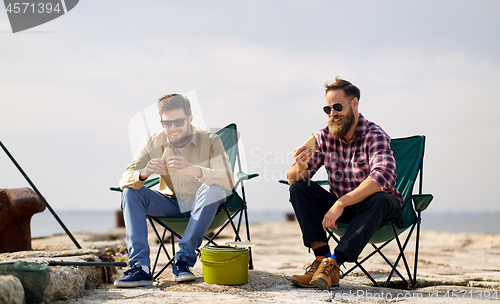 Image of happy friends fishing and eating sandwiches