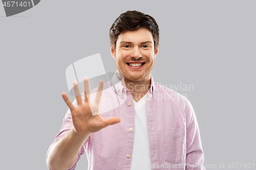 Image of young man showing five fingers over grey