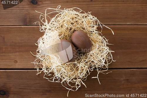 Image of chocolate eggs in straw nest on wooden background