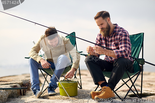 Image of friends adjusting fishing rods with bait on pier