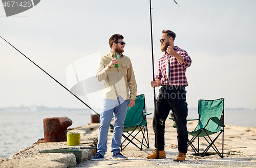 Image of happy friends with fishing rods and beer on pier