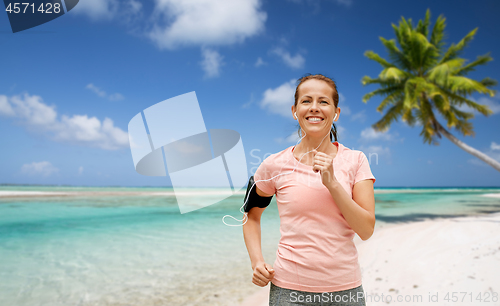 Image of woman with earphones and armband running on beach