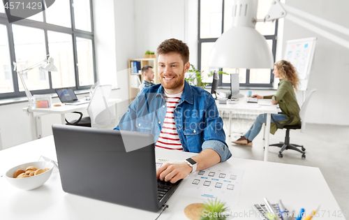 Image of smiling creative man with laptop working at office