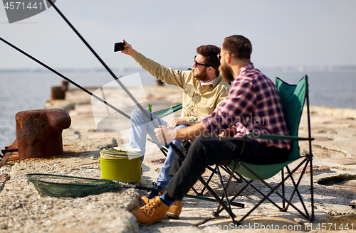 Image of friends fishing and taking selfie by smartphone