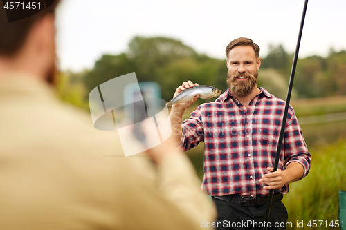 Image of friend photographing fisherman with fish at lake