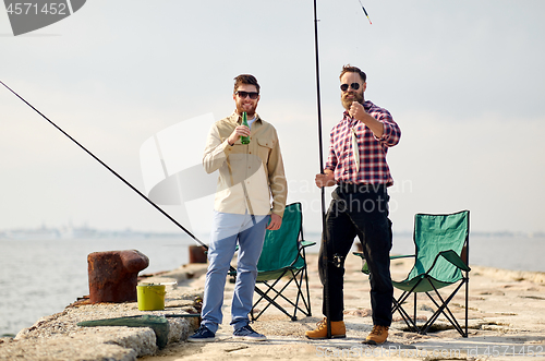 Image of happy friends with fishing rods and beer on pier