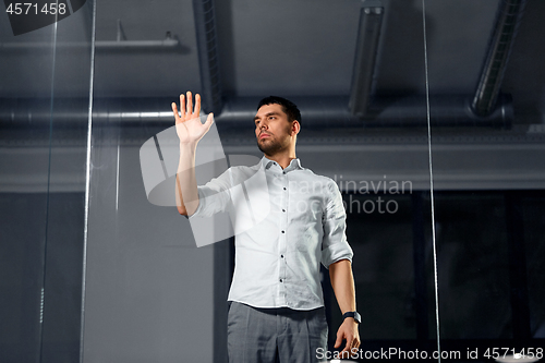 Image of businessman touching glass wall at night office