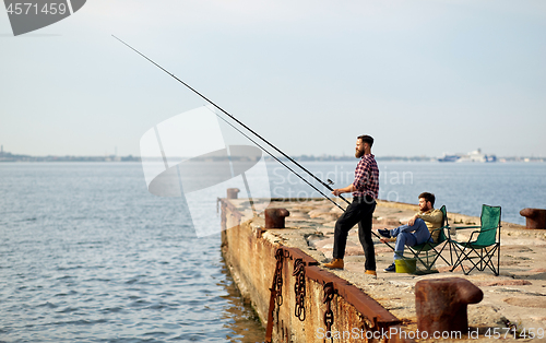 Image of happy friends with fishing rods on pier