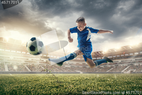 Image of Young boy with soccer ball doing flying kick at stadium