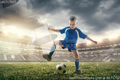 Image of Young boy with soccer ball doing flying kick at stadium