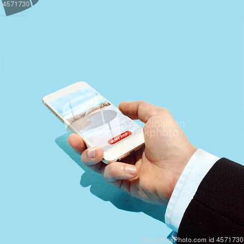 Image of Hand holding smartphone with hotel booking application on the beach and blue sky