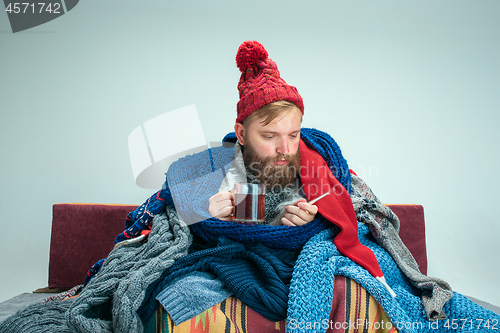 Image of Bearded Man with Flue Sitting on Sofa at Home. Healthcare Concepts.