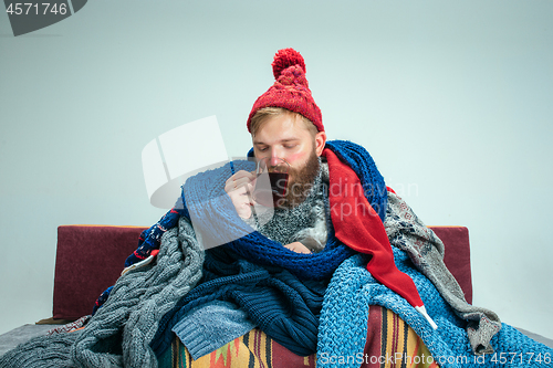 Image of Bearded Man with Flue Sitting on Sofa at Home. Healthcare Concepts.