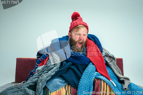 Image of Bearded Man with Flue Sitting on Sofa at Home. Healthcare Concepts.