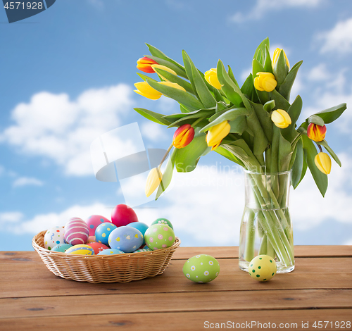 Image of colored easter eggs in basket and flowers over sky