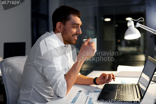 Image of businessman with coffee and laptop at night office